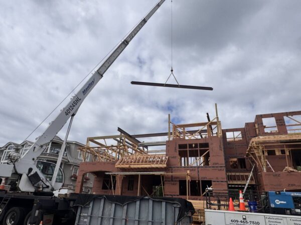 Manitex 40124SHL boom truck lifting a steel beam over a framed home