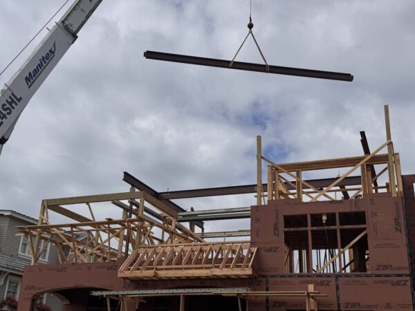 Manitex 40124SHL boom truck lifting a steel beam over a framed home