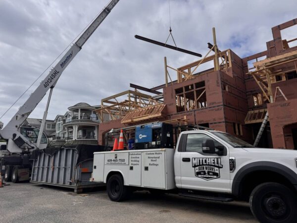 Manitex 40124SHL boom truck lifting a steel beam over a framed home
